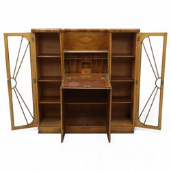 Art Deco walnut bureau bookcase, top with moulded and rounded edges and stepped front profile, central shelf, and fall-front bureau section with vertical and horizontal pigeon holes and a small drawer, above two cupboard doors and flanked by two tall glazed display cabinets with single doors and geometric sunburst design astragal glazing bars enclosing three shelves, raised on cavetto shaped plinth base 