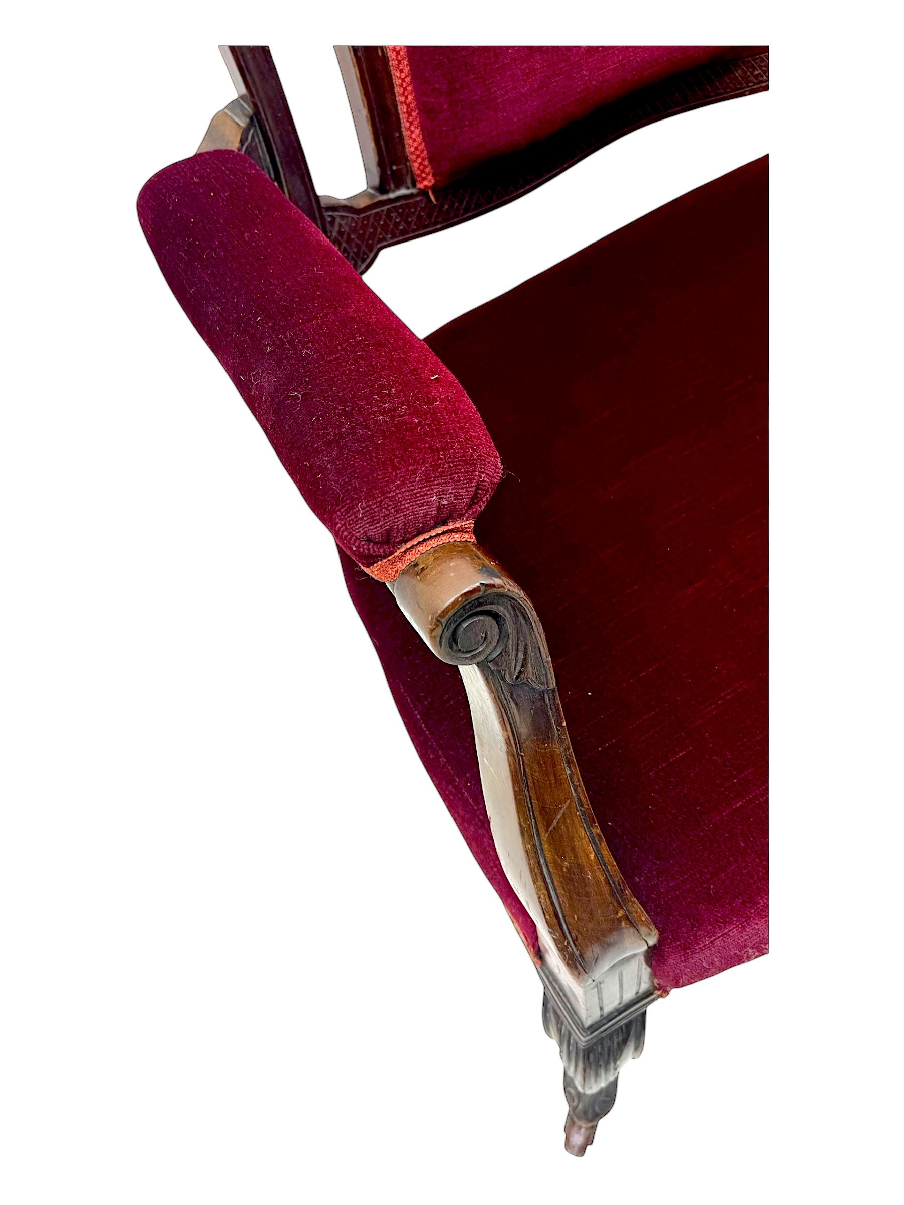 Late Victorian stained beech framed sofa, the backrests, seat and padded arms upholstered in deep red fabric, carved crest rail with scroll and foliate motifs supported by carved uprights, on cabriole supports with leaf carvings terminating in castors