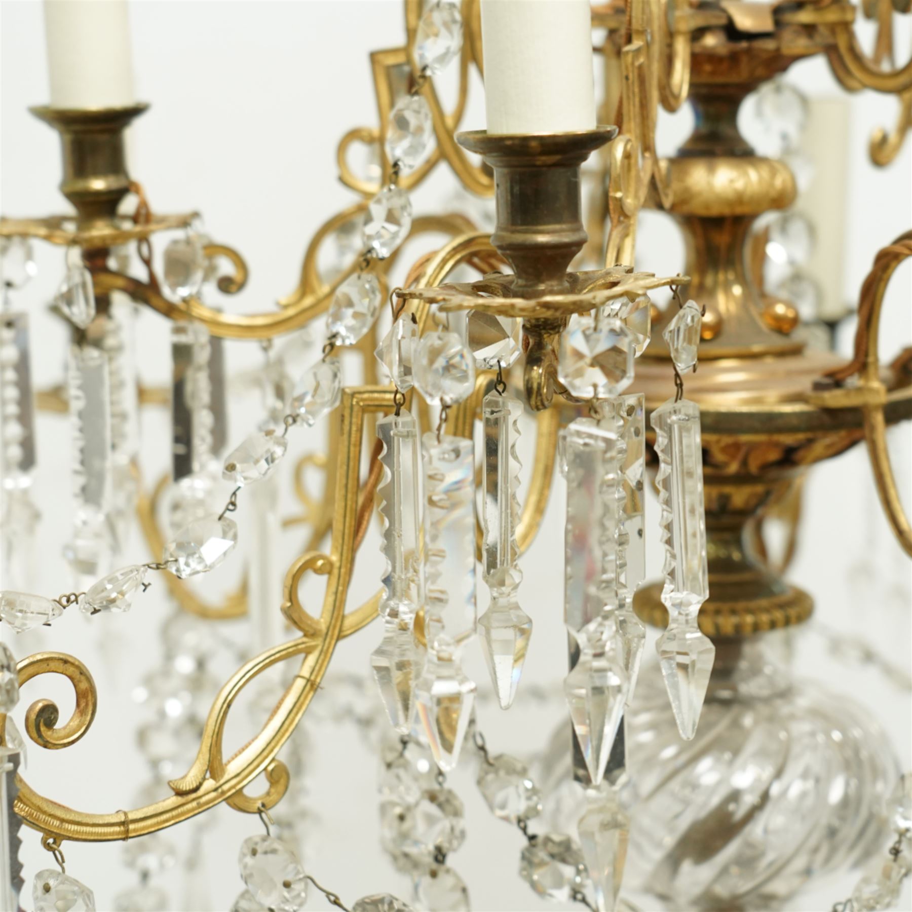 Late Victorian gilt bronze mounted crystal chandelier, ceiling rose above shaped top of trailing swags, glass crystal droplets, beneath rising curled branches and glass beads tapering down to five candle sconces, inside circular bezel fitted with drops and glass twist fluted stem, supported with an internal metal shaft above a rococo style stem holding double branches, and similar styled branches, with twelve branches fitted with candle holders and drip trays with crystal drops and cut crystal spears, the underside festooned with crystal glass swags and a bulbous fluted glass terminal and shaped finial with crystal glass swags attached to the branches, the base with pear shaped droplet graduating to the centre, wired for electricity 