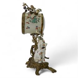 French- early 20th century 8-day Chinoiserie brass and porcelain mantel clock in the 18th century style, brass base with splayed feet profusely decorated with clusters of painted porcelain flowers and two decoratively painted Chinese foo dogs, movement enclosed in a circular porcelain movement case illustrated with birds of paradise and oriental motifs, with a white enamel dial Arabic numerals, minute markers, pierced gilt hands and a floral swag, rack striking Parisian movement striking the hours and half-hours on a bell. With a visible sunburst pendulum and key.