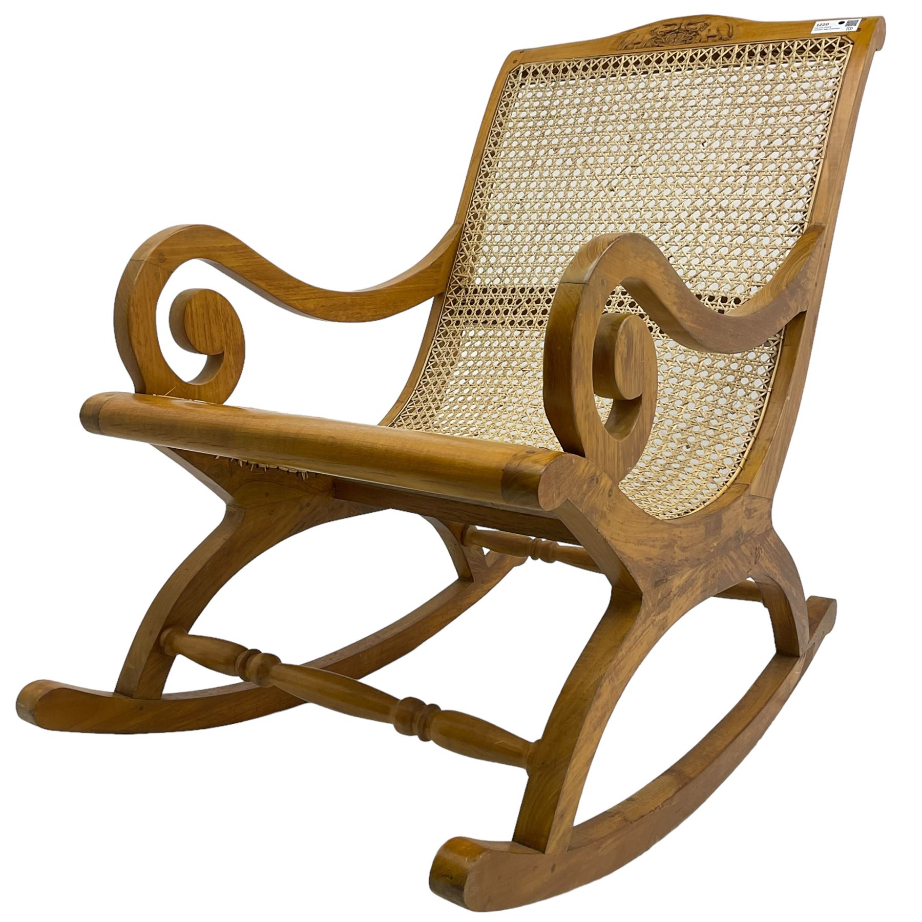 Late 20th century teak framed plantation style rocking chair, cresting rail carved with two elephants with upraised trunks, cane back and seat with scrolled arm terminals, rocker base united by turned stretcher