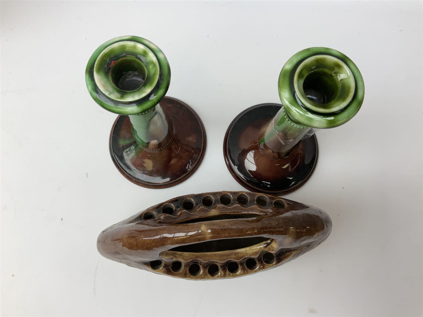 Linthorpe pottery vase with crimped rim and ovoid body, Linthorpe jug with high loop handle and crimped spout, a pair of candlesticks with a green, brown glaze and other similar pottery 