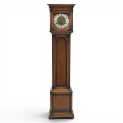 Early 20th century oak longcase clock, square brass dial with engraved foliate spandrels and centre, silvered Roman chapter ring with Arabic minute track, Westminster chime movement, the plain case with glazed arched trunk door and moulded plinth