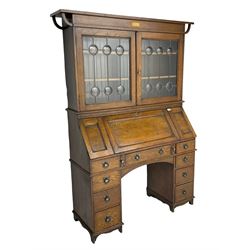 The Britisher Desk - early 20th century oak bureau cabinet, the raised cabinet enclosed by lead glazed doors, fall front with hinged side panels revealing fitted interior, twin pedestal base, fitted with nine drawers
