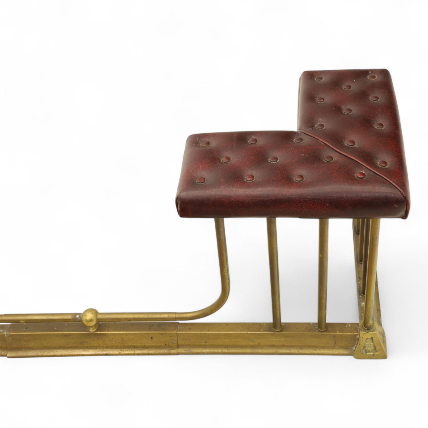 Late Victorian brass and cast iron club fender, burgundy leather buttoned seat pads, secured by bar uprights at the front and back, and a cross stretcher held in place by further bar uprights on a chamfered platform base, circa 1890, internal base dimensions 127cm 