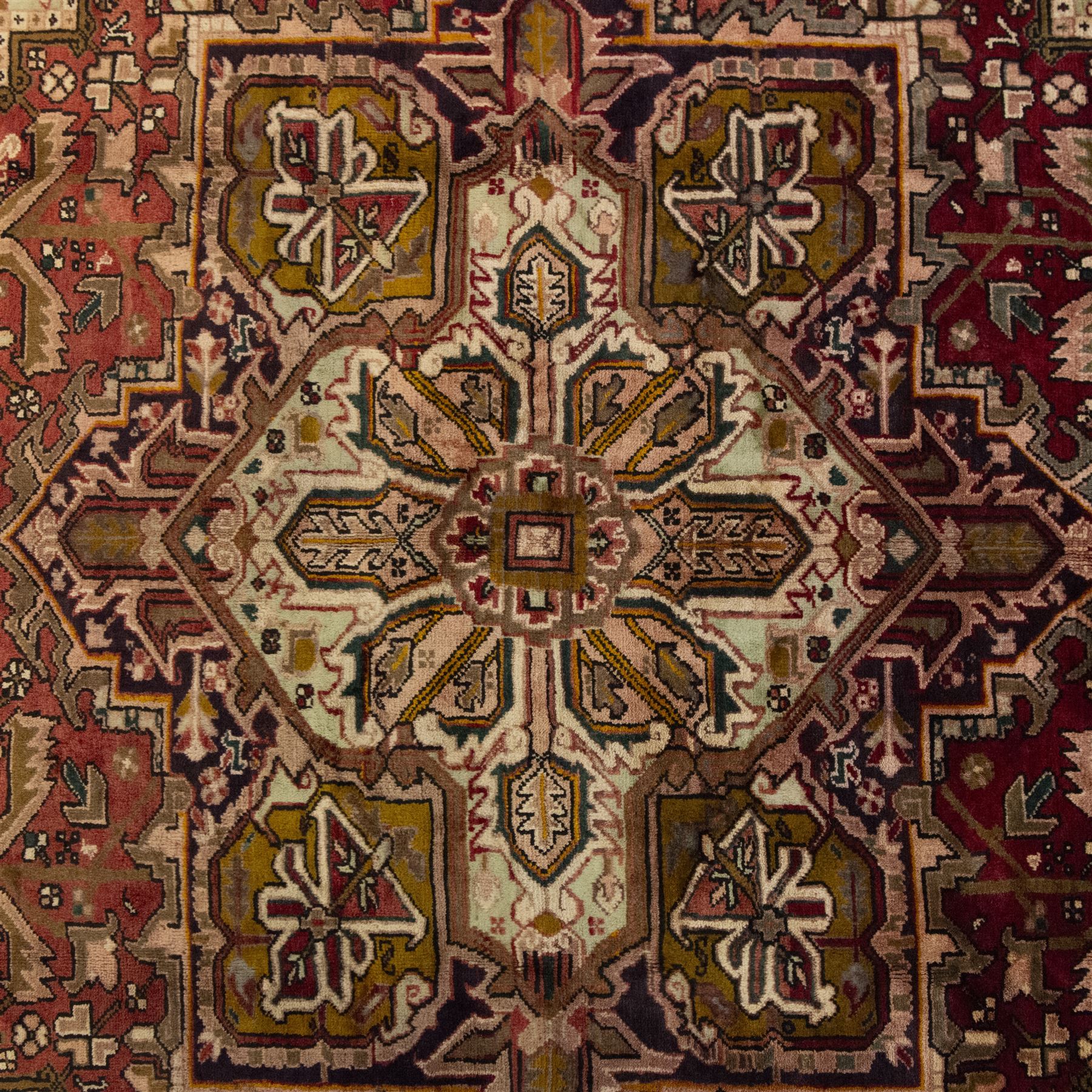 Northwestern Persian Heriz carpet, crimson ground and soft green field, with bold terracotta stepped medallion with angular spandrels and geometric motifs within a broad palmette and vine border 