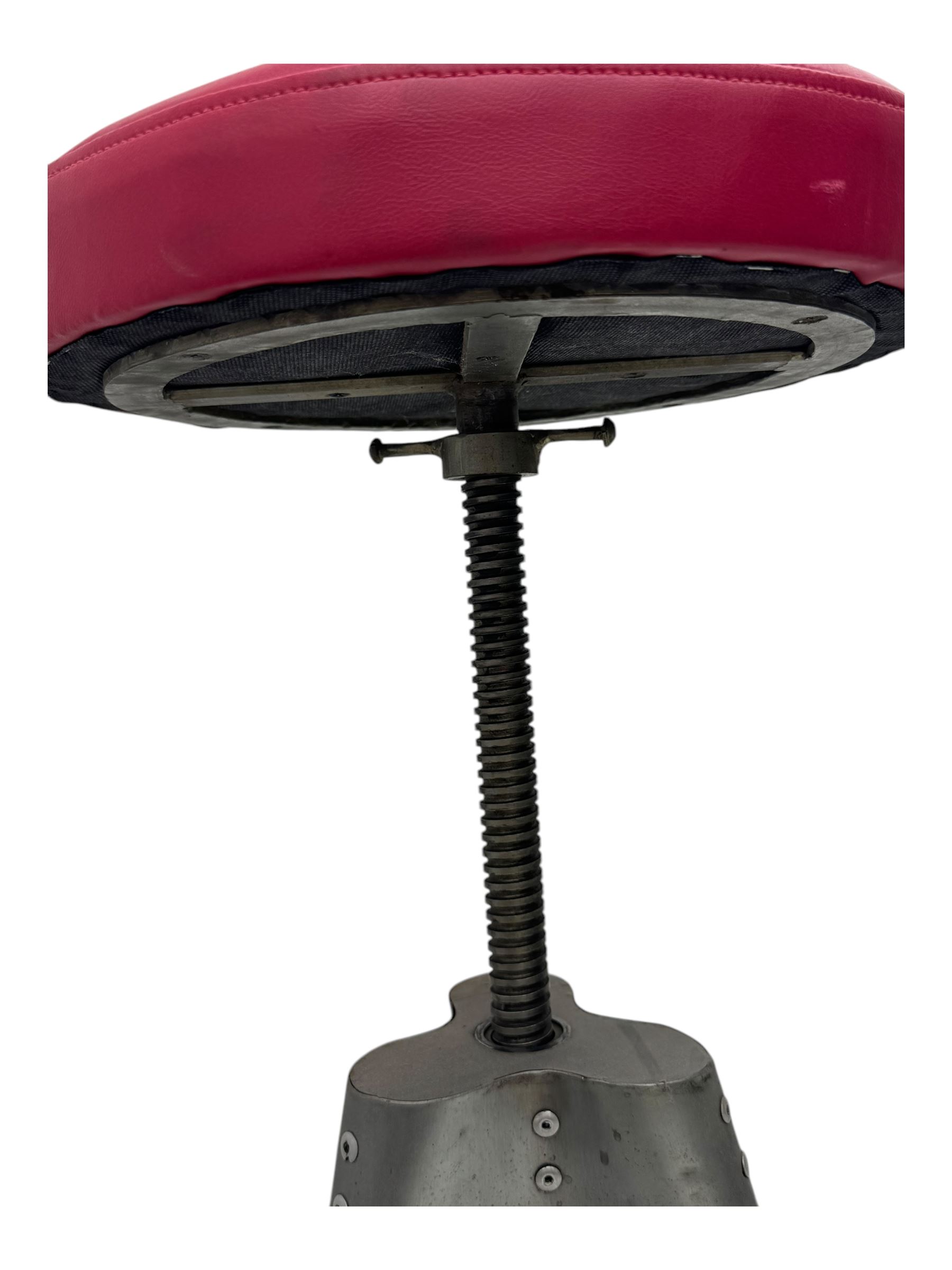 Contemporary industrial design riveted metal table, by repute fashioned from salvaged aeroplane parts, with a circular glass top on a tripod base, accompanied by three adjustable stools upholstered in burgundy
