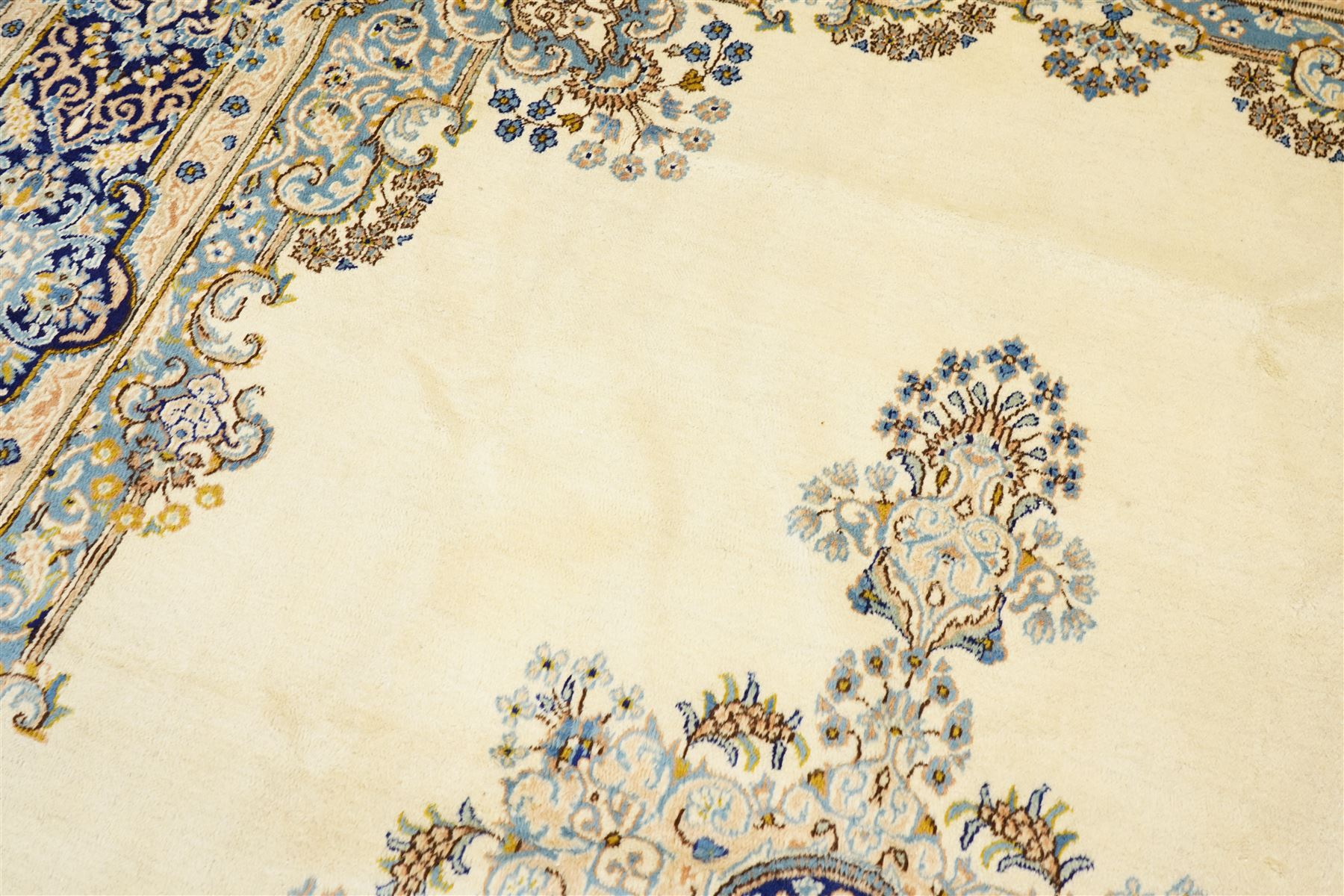 South East Persian Kirman hand-knotted carpet, ivory field with central floral medallion in tones of cobalt and pale blue, issuing scrolling vinery and palmettes, conforming spandrels, main border with scrolling foliage and stylized palmettes, framed by multiple guard borders, with cotton fringe ends 
