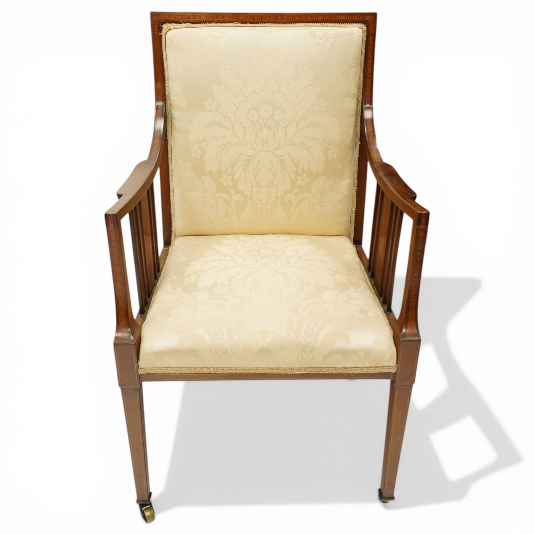 Arts & Crafts period inlaid mahogany framed armchair, swept arms with satinwood-strung supports over back and sprung seat upholstered in cream foliate damask fabric, on square tapering supports with castors