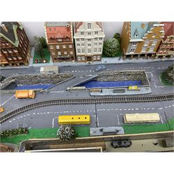 Table top 'N' gauge continental scenic layout as a split level town with various loops of track, station with numerous platforms, engine shed, assorted buildings, roads with motor vehicles and figures, tunnels, trees, river with bridge, tram depot etc 122 x 52cm
