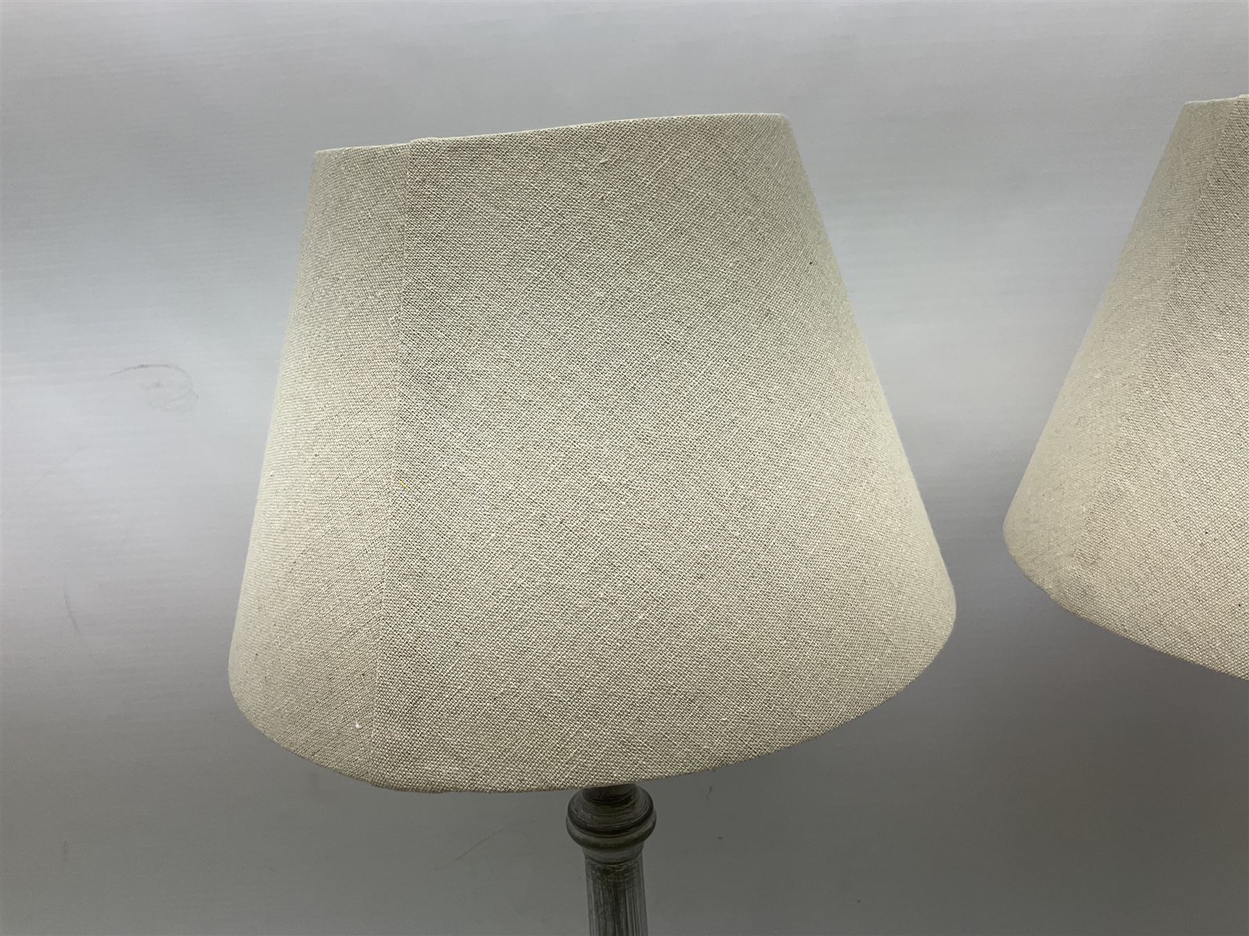 Pair of composite grey washed table lamps with a slender column upon a circular foot with natural linen shades