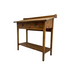 Stained pine clerks desk or table, raised back and sloped writing surface over single fall-front cupboard, raised on square supports united by under-tier