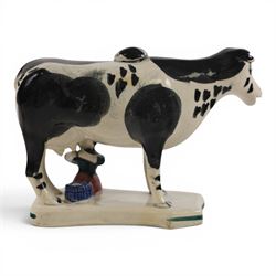 Three Staffordshire cow creamers, one with treacle glaze, the other two painted black and white with a seated figure of a milkmaid, H14cm