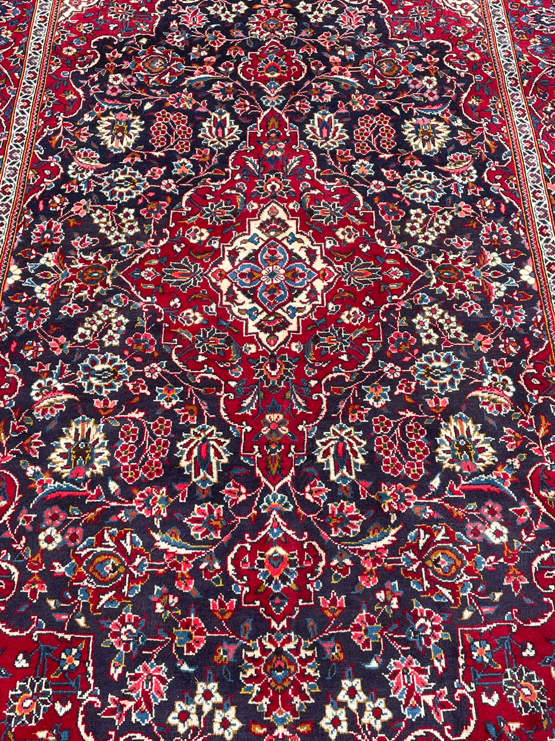 Persian indigo ground rug, the central crimson pole lozenge medallion surrounded by interlacing floral patterns, the main border with repeating plant motifs connected by scrolling branches