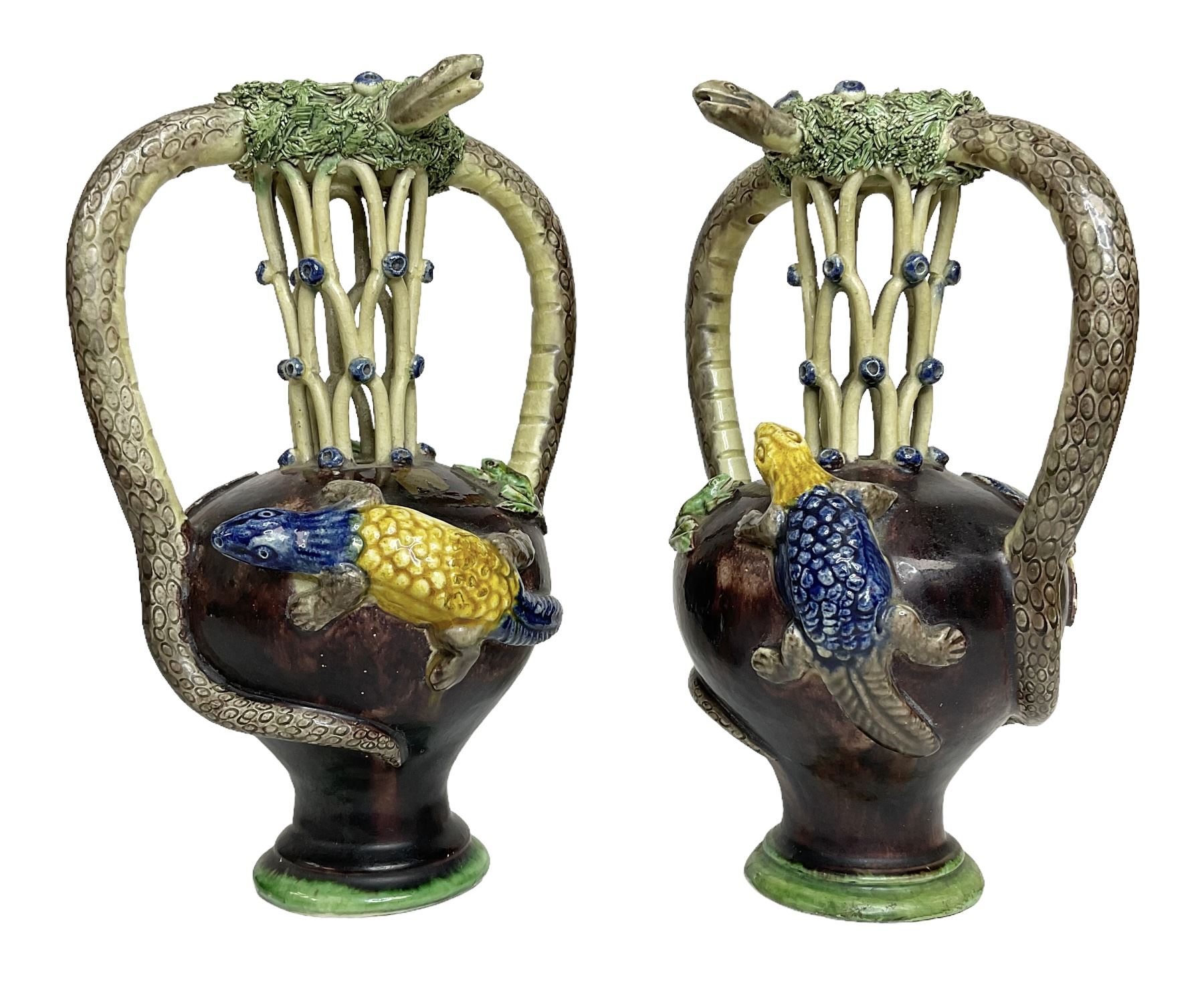 Pair of 19th century Portuguese Palissy style Majolica puzzle jugs, attributed to Manuel Mafra, with mossy rim and pierced lattice neck, twin handles in the form of snakes and the body decorated with frogs, lizards, and moths on a mottled brown glazed ground, unmarked, H20cm