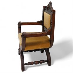 Victorian heavily carved oak X-framed throne chair, the cresting rail carved with mask and curling foliage, upholstered in mustard fabric, the arms and frame carved with scrolling foliage, united by turned stretchers 