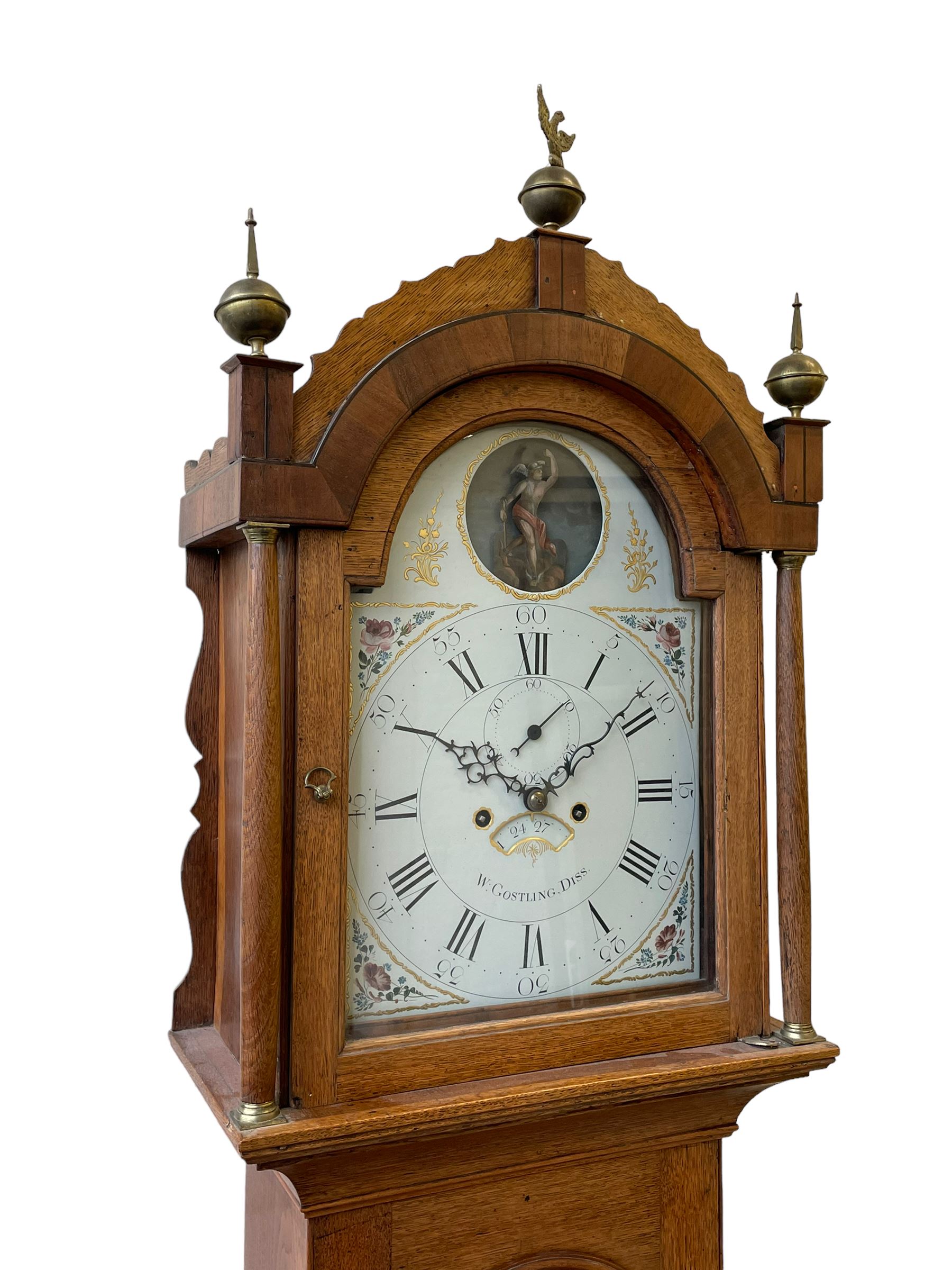 William Gostling of Diss  (Norfolk)-  Late 18th century 8-day oak longcase clock c1780-90, break arch top with scalloped cresting and three brass finials, glazed break arch hood door flanked by turned pilasters with brass capitals, trunk with a long trunk door and rounded top on a square plinth with an applied and shaped skirting, early painted Wilson of Birmingham dial with Roman numerals and five minute Arabic's, matching steel hands and second pointer, arched square ended calendar aperture with date disc behind, floral spandrels within gesso borders and a painted rocking automaton representing Mercury to the break arch, dial pinned via a false plate to a weight driven rack striking movement with a recoil anchor escapement, striking the hours on a cast bell. With pendulum weights and key. 
William Gostling (II) is recorded as working in Diss from 1774 to 1797, succeeded by widow Anne and son George . The dial of this clock is illustrated and discussed in detail in M.F. Tennants book 