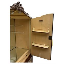 Early 20th century walnut veneered cocktail cabinet, shaped and carved foliate pediment above a pair of arched panelled doors with figured veneers and ornate cast escutcheons, interior is mirrored on the base and back, slide out mirrored shelf, flanked by foliate carved uprights, over a conforming lower cabinet, all raised on shaped apron and scroll carved cabriole feet