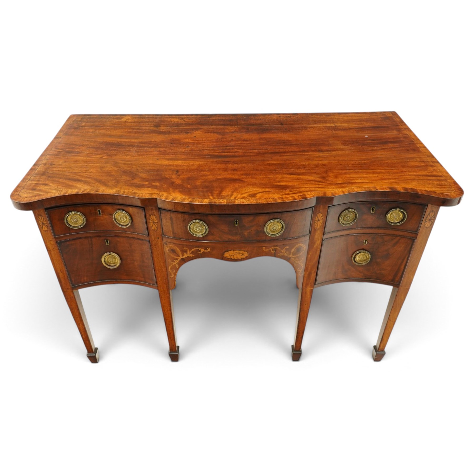 George III inlaid mahogany serpentine sideboard, the shaped top with crossbanding and satinwood stringing, fitted with central bow-front cock-beaded frieze drawer over a shaped apron inlaid with paterae, shell motifs and scrolling foliage, flanked by a deep right-hand drawer and two drawers to the left, raised on square tapering supports with spade feet