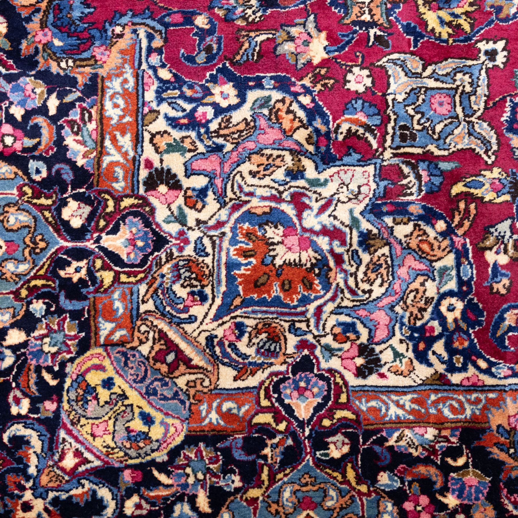Large North East Persian Meshed hand-knotted carpet with signature, raspberry red field with central shaped cusped medallion, densely decorated with intricate arrangement of scrolling vines, and florals designs within conforming spandrels and a dark ground border richly ornamented with stylized flowers, vase and bird ornamentation, enclosed by guard stripes, with cotton fringe ends