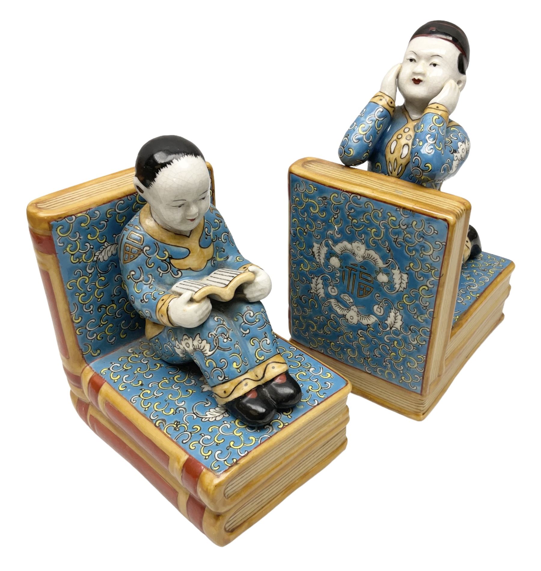 Pair of 20th century Chinese figural bookends, modelled as children in traditional blue dress sat reading and kneeling upon stacks of books, H22cm