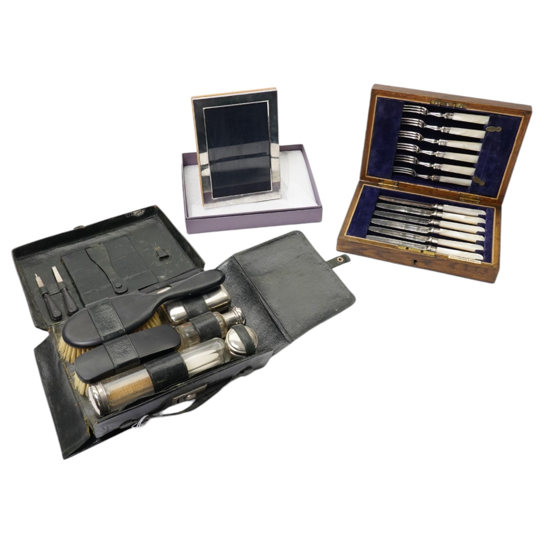 Set of six dessert knives and forks with silver collars and mother of pearl handles, silver plated photograph frame and travelling toilet set in leather case