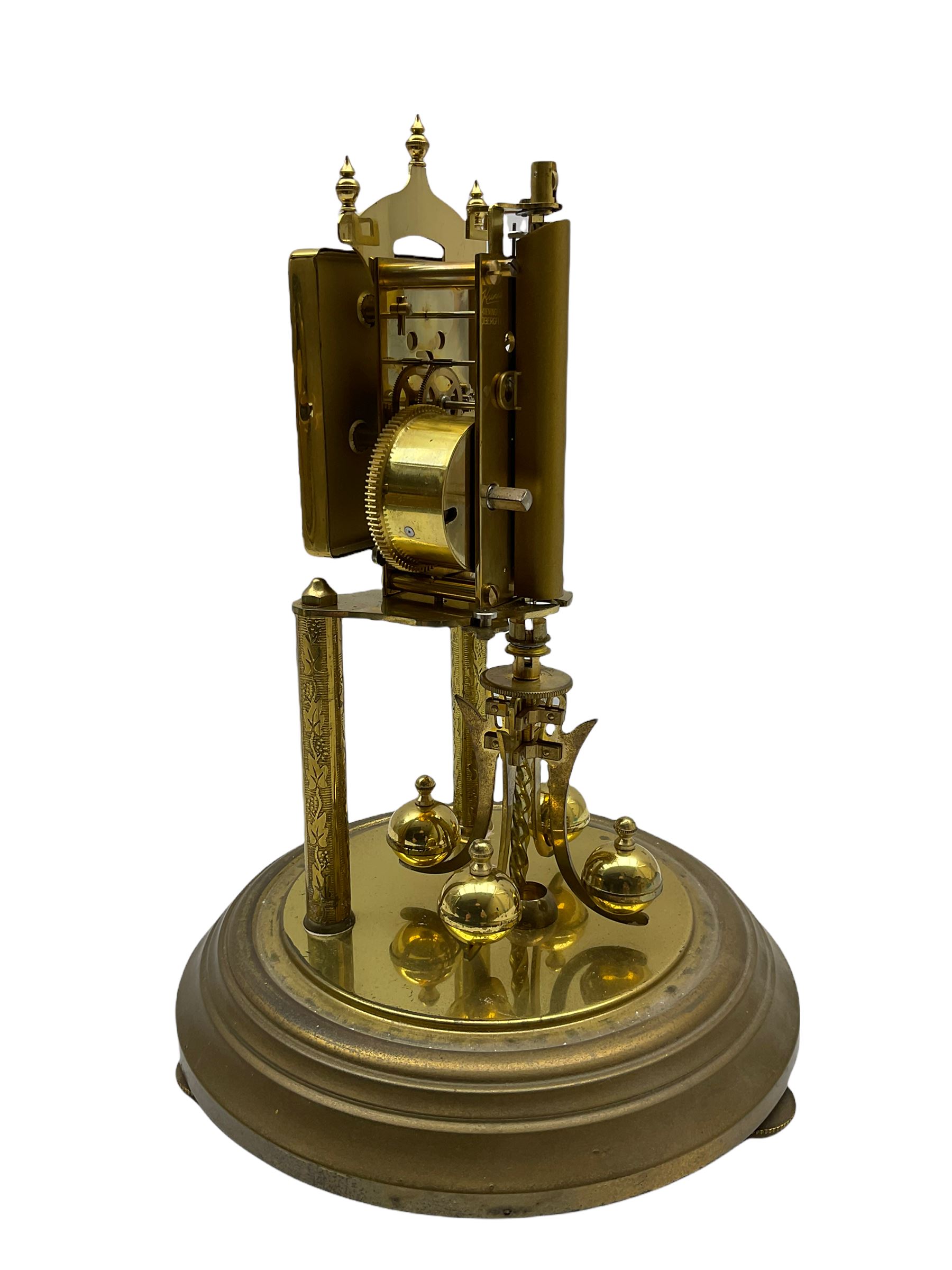 A “Kundo” 400-day torsion clock made by the 20th century German manufacturer Kieninger & Obergfell, with a  decorative square dial and pierced steel hands within a foliate bezel, on a circular base with adjustable feet, four-ball rotary pendulum under a glass shade. 
H30cm
