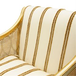 Louis XV design cream painted and parcel-gilt bergere armchair of large proportions, high scrolled back over canework arms, upholstered in striped fabric with over-stuffed loose seat cushion, on fluted supports