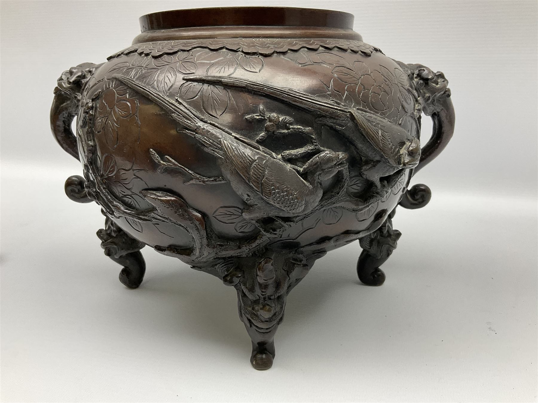 Japanese bronzed koro, the body of globular form with twin cast zoomorphic mask handles, decorated in relief with birds upon blossoming branches, against a ground incised with rushes and peonies, the flat toped domed cover with pierced band and surmounted by a cast figure of a Foo dog, the whole upon three zoomorphic mask feet, with impressed character type mark beneath, H35.5cm