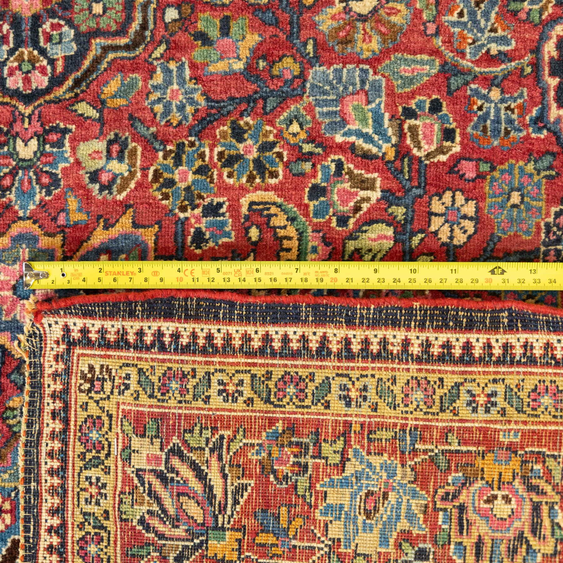 Persian Sarouk rug, richly decorated with an elaborate central medallion of palmettes and stylized floral motifs in indigo, ivory, and pastel tones on madder red ground, framed by spandrels, with a broad border of flowering palmettes and serrated leaves between a narrow floral guard border, fringe removed 