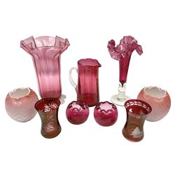 Group of cranberry glass, to include trumpet vases, with crimped decoration, jug with a clear glass handle, large vase with clear feet and crimped rim, and two ruby glass beakers