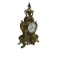 French - late 19th century 8-day gilt brass mantle clock surmounted by an urn, with a waisted case and baroque decoration raised on four splayed feet, with a glazed bezel, enamel dial with Roman numerals, five minute Arabic's and gothic steel hands, count wheel striking movement, striking the hours and half-hours on a bell. With pendulum.