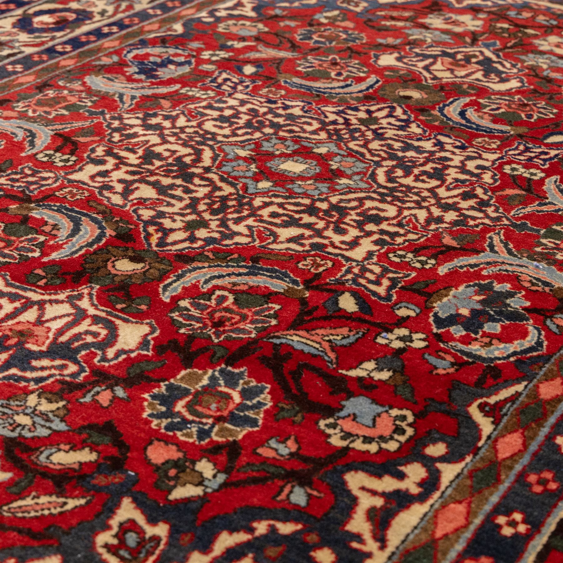 Central Persian Isfahan hand-knotted rug, madder red field, with elaborate central medallion with pendants and scrolling arabesques, palmettes and stylized floral sprays arranged in a densely ornamented ground of classical Safavid inspiration, ivory border with a continuous vine scroll of palmettes and rosettes, flanked by multiple guard stripes in navy and red with geometric and floral motifs, with cotton fringe ends 