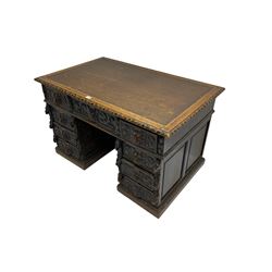 Late 19th century Gothic revival carved oak twin pedestal desk, rectangular top with inset writing surface and carved edges, central frieze drawer flanked by eight drawers, all with green man carved handles and extending trailing foliage, carvings of pineapple and lion mask corbels, the pedestals with panelled sides and back, on plinth bases