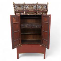 Early 20th century Chinese lacquered marriage cabinet, of rectangular form in red lacquer, fitted with double doors centred by circular brass lock plate and drop handles, the interior with shelves and two short drawers, cornice and apron with giltwood foliate and figural carving, together with an elaborately pierced and gilded wooden cresting panel carved with scenes of figures within pavilions and stylised dragons