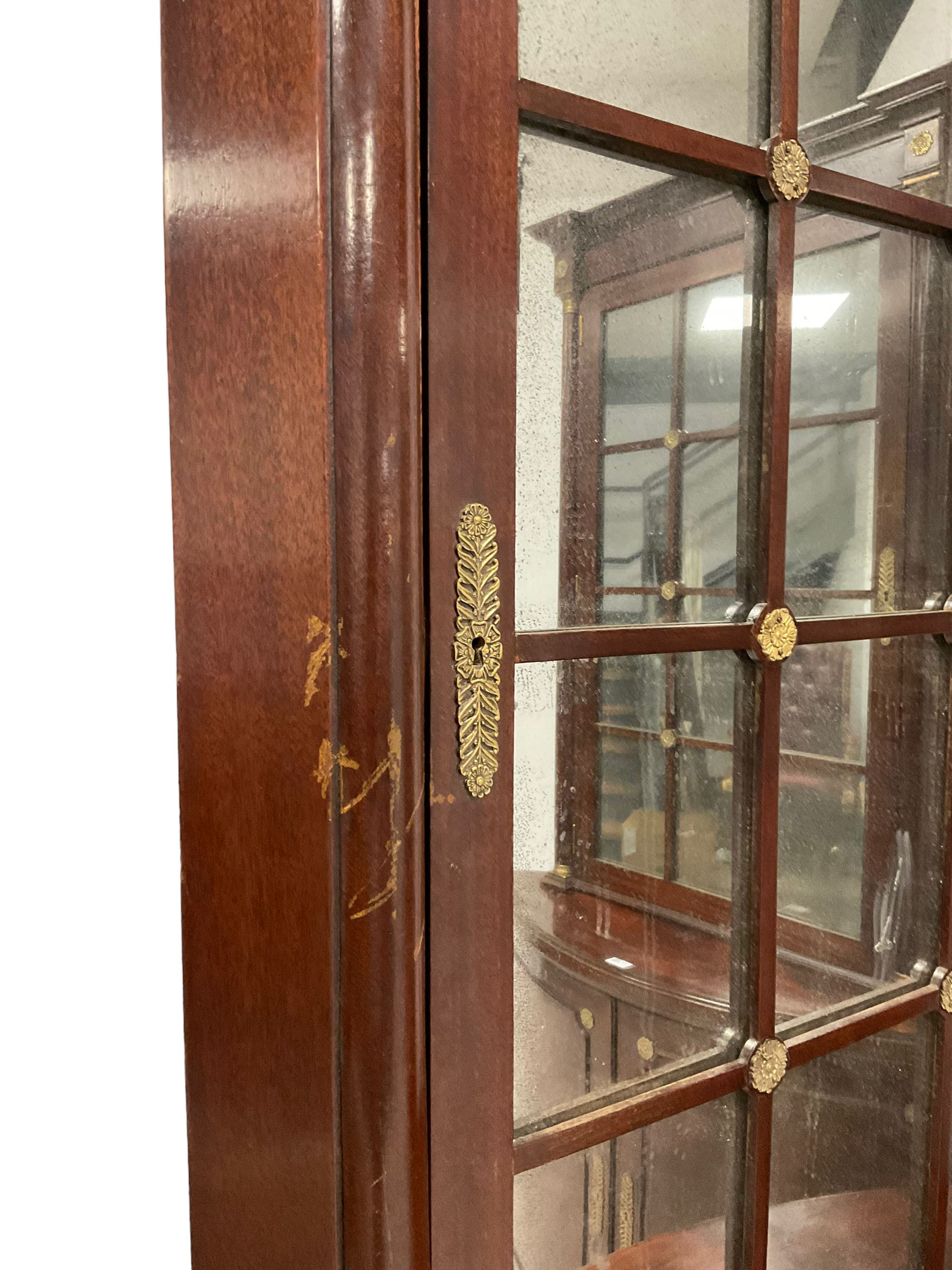 Pair of French Empire design corner cabinets, the straight-front upper section with canted corners and applied half-column pilasters, enclosed by mirror glazed door, the bow-front lower section enclosed by two doors with applied mouldings, mounted by cast metal floral rosettes, skirted base with cast gilt metal hairy paw brass feet