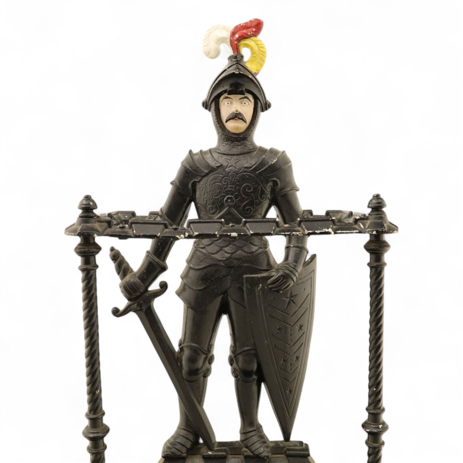 Early 20th century painted cast iron hall stand, formed as a standing armoured figure with red and yellow feathered crest, twin rails and integral drip tray with castellated edge