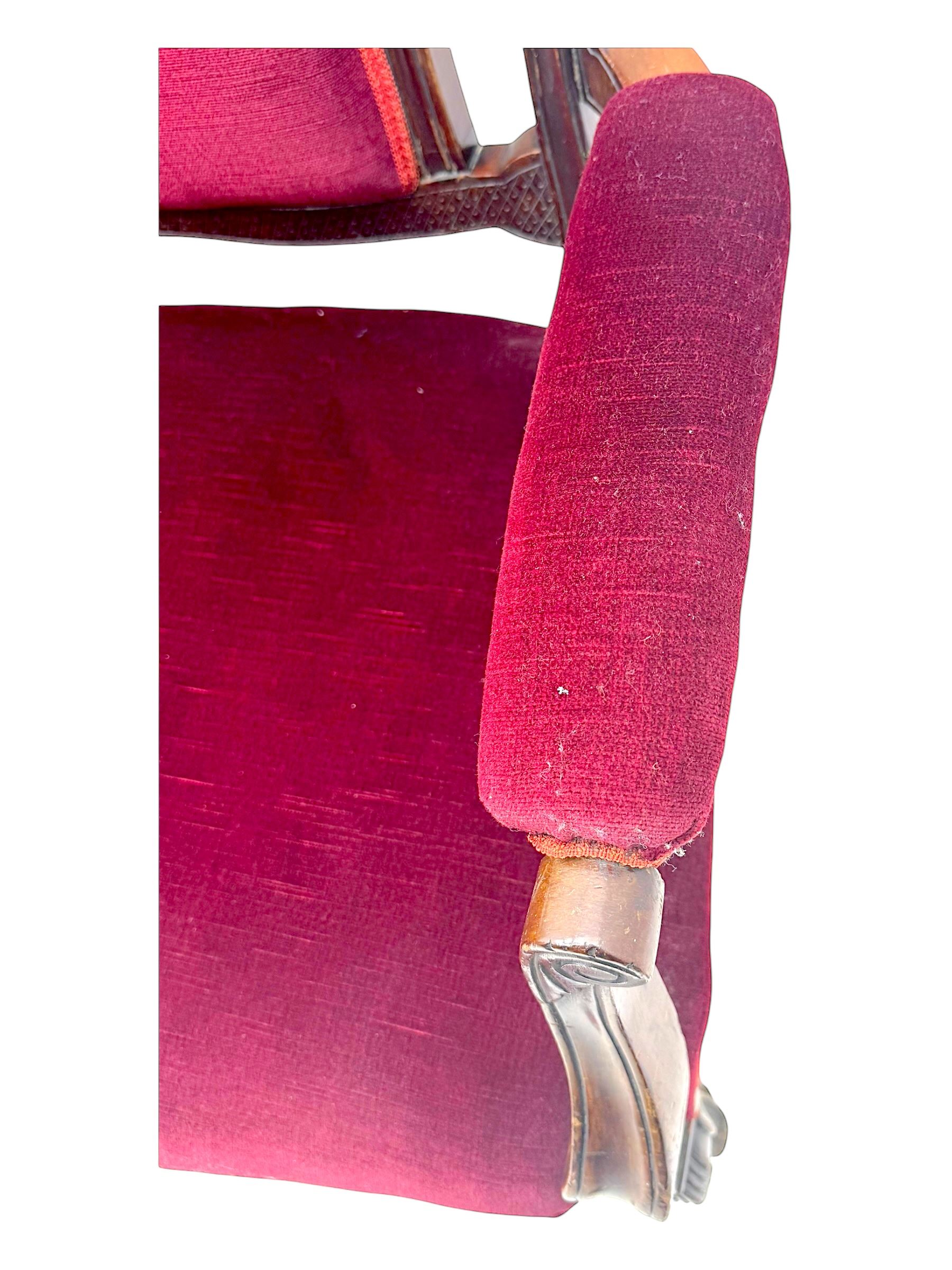 Late Victorian stained beech framed sofa, the backrests, seat and padded arms upholstered in deep red fabric, carved crest rail with scroll and foliate motifs supported by carved uprights, on cabriole supports with leaf carvings terminating in castors