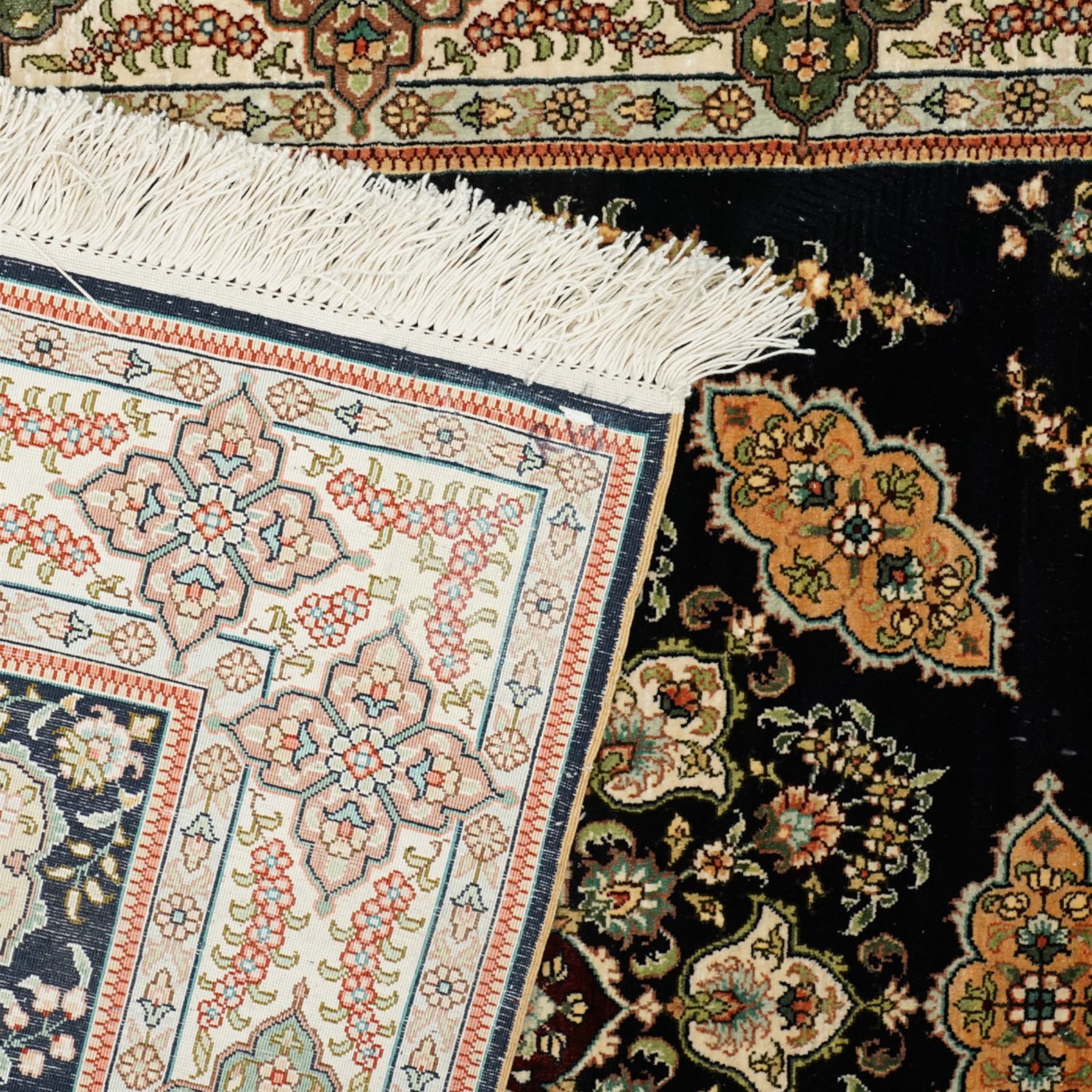 Persian-inspired Qom-style silk rug, deep indigo ground, profusely decorated with foliate motifs and a central medallion, with cotton fringe ends 
