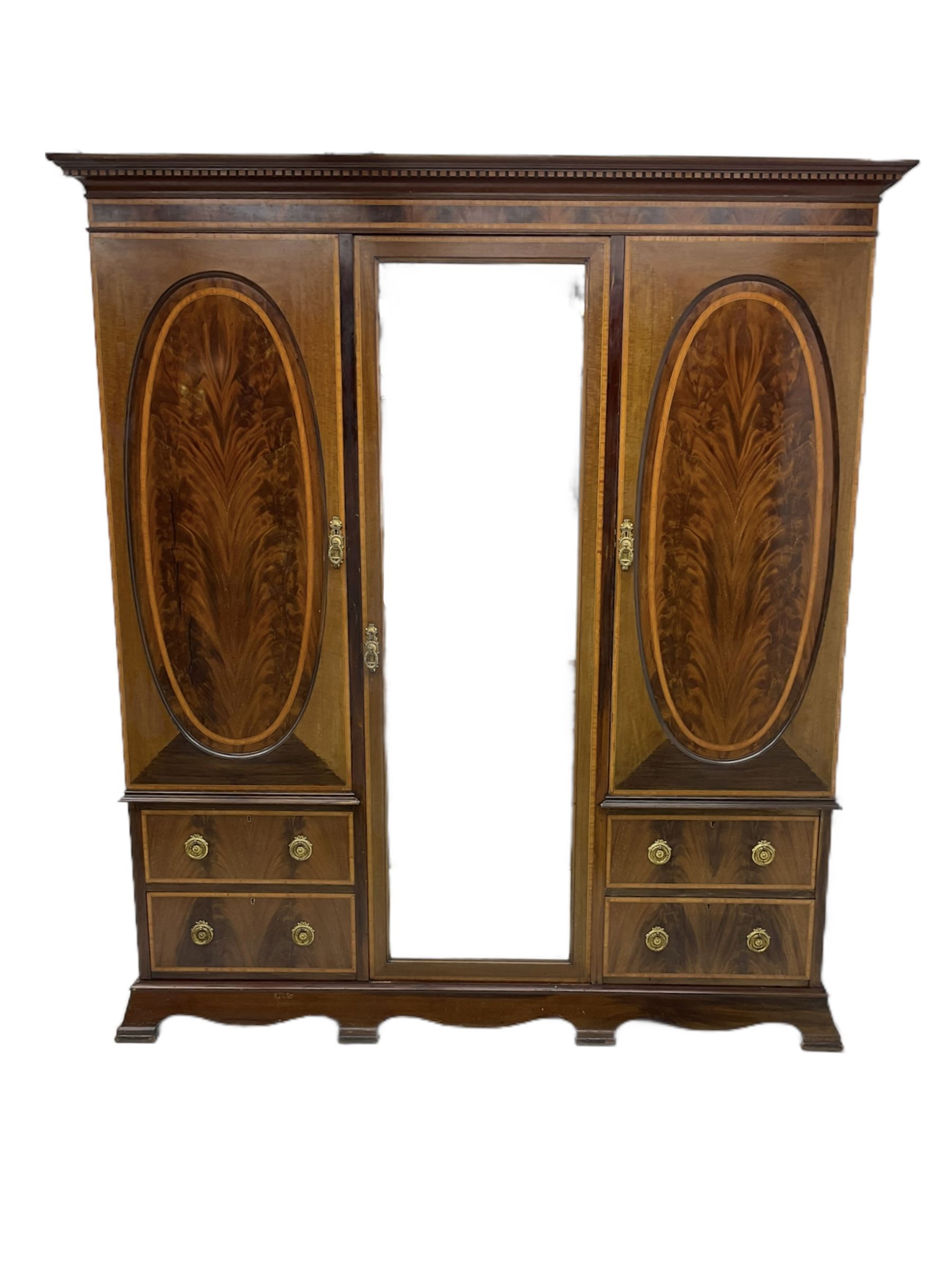 James Shoolbred & Co. London - Edwardian inlaid mahogany triple combination wardrobe, projecting dentil cornice over bevel glazed door, two figured oval panelled doors and four drawers, the central compartment fitted with linen slides and drawers, satinwood banding, on base with shaped apron and bracket feet, with enamel plaque 