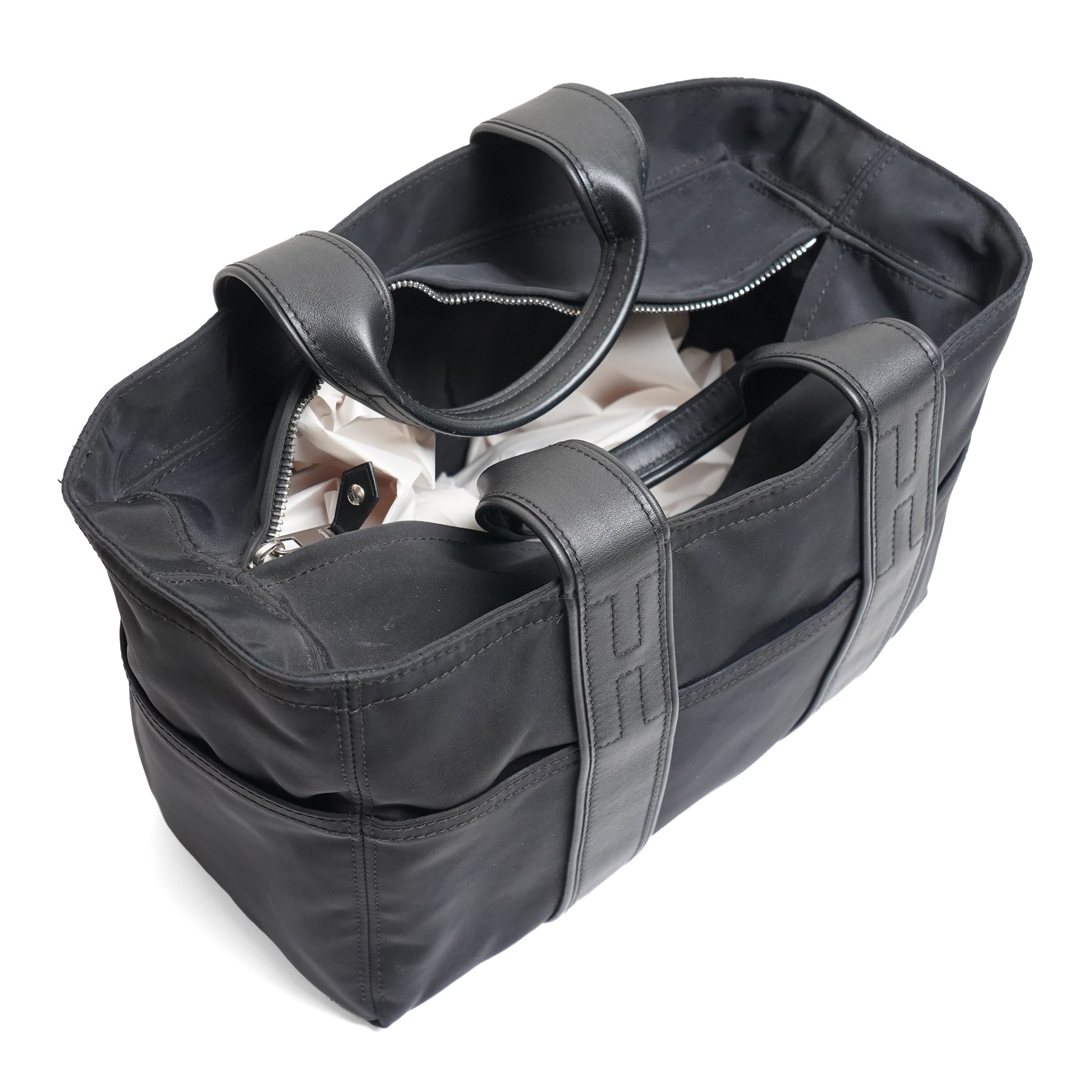 Hermès - Acapulco PM tote bag in black Toile Chevron canvas with black leather trim, the rectangular body with twin flat handles incorporating stitched H details, top zip fastening and eight exterior slip pockets, opening to a black nylon-lined interior with zip pocket, palladium-tone hardware, stamped Hermès Paris Made in France, with original Hermes dust bag