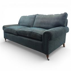 Late 20th century three seat sofa upholstered in green fabric, with gently rounded scroll arms, loose seat and back cushions, raised on turned wooden legs with castors, rear splayed legs