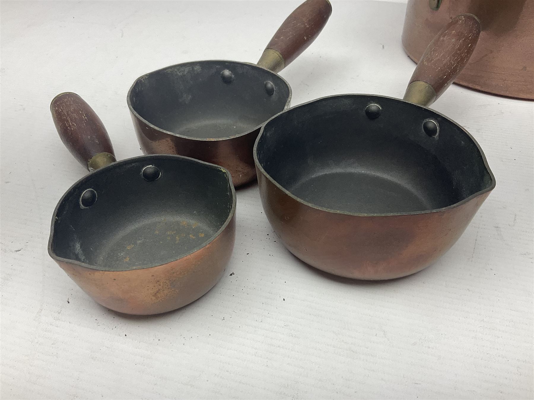 Four Victorian copper moulds, together with a graduating set of copper pans with wooden handles and finials to covers, largest pan 