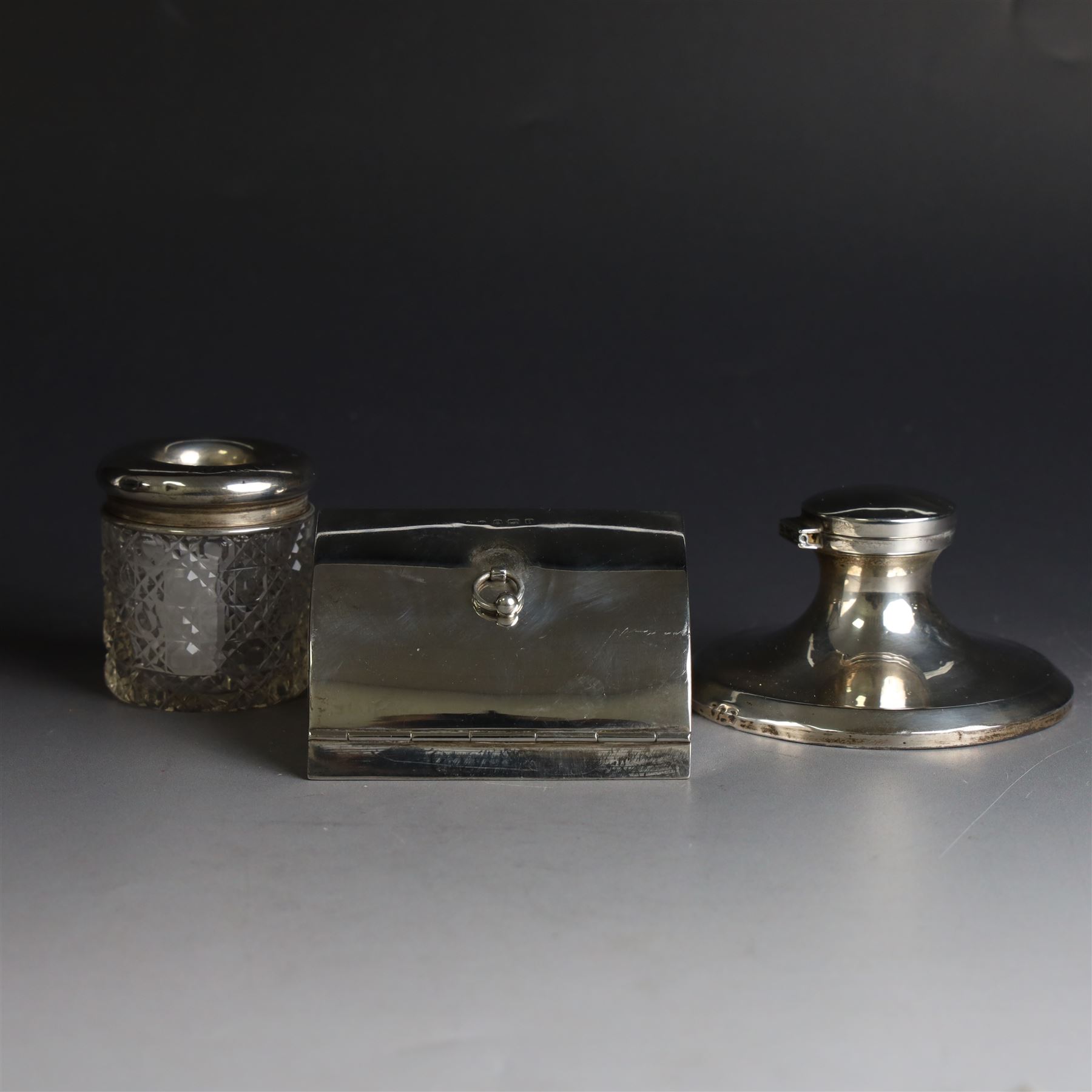 Edwardian silver fall-front ring box with loop handle, opening to reveal velvet interior with five ring spaces, hallmarked Deakin & Francis, Birmingham 1907, together with a cut glass jar with silver lid inscribed 'Hair Tidy' and a silver mounted capstan inkwell, both hallmarked 