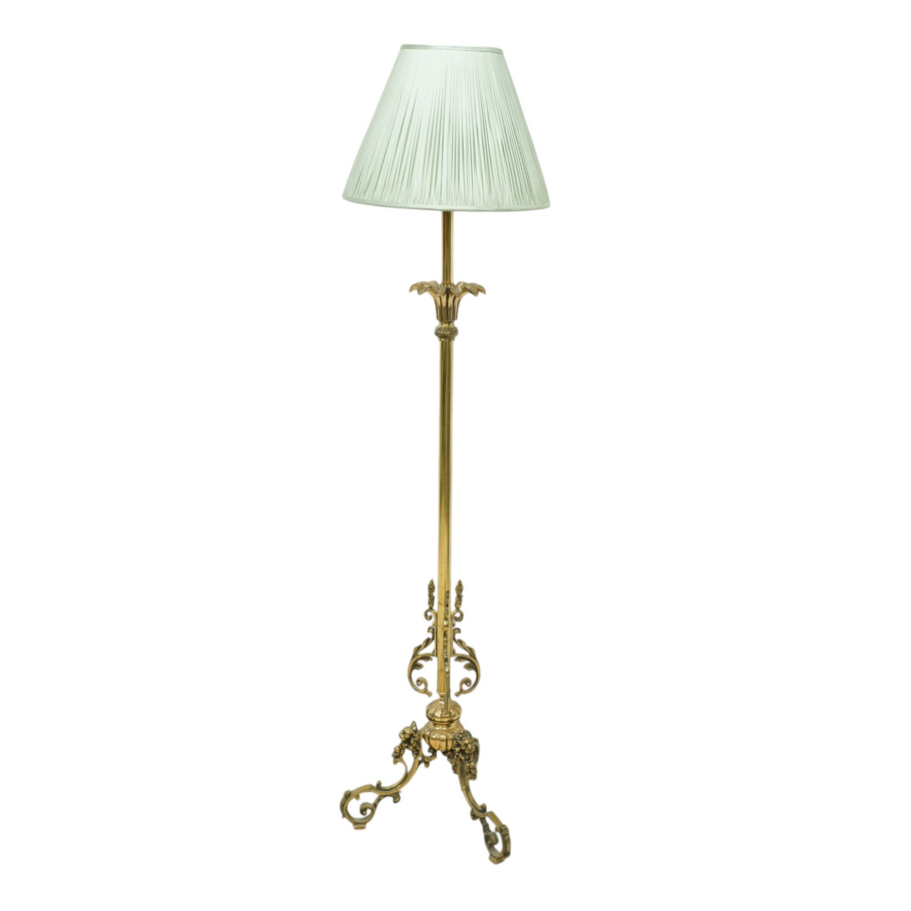 Late Victorian brass standard lamp with shade, slender column with blooming lotus leaf floral base with raised acanthus leaf scrolls above a tripod stand with scroll legs 