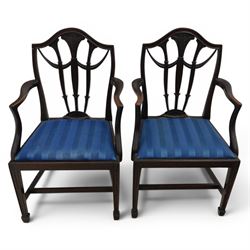 Set of eight George III style mahogany dining chairs, comprising two carvers and six singles, each with shaped top rail above pierced splay carved with feathers, with drop in stuffover seats upholstered in blue striped fabric, raised upon square tapering legs joined by stretchers, together with a mahogany twin pedestal dining table, the oval top with central leaf raised upon turned columns and splayed reeded legs terminating in lion paw feet and brass castors, 