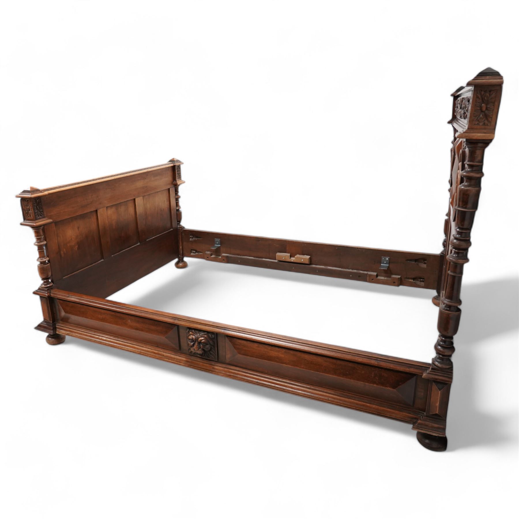 Late 19th century French walnut double bedstead, the panelled headboard with curling foliage carved frieze over concentric turned roundels and faceted mounts, lion mask carved rails with applied panelled mounts, matching footboard with lower carved lion mask 