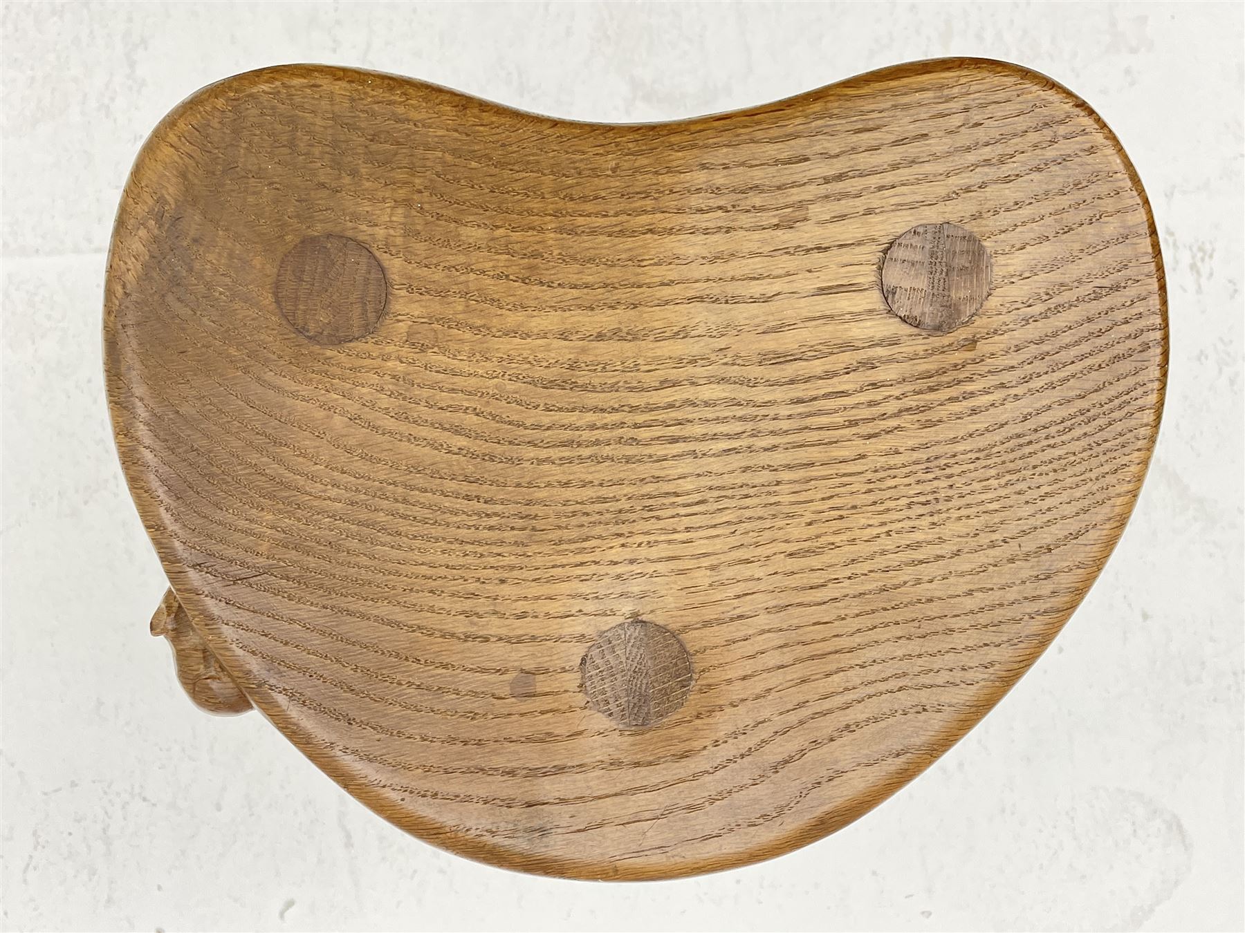 'Mouseman' oak three legged stool with dished kidney shaped seat, tapered octagonal supports, with carved mouse signature, by Robert Thompson of Kilburn 