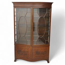 Edwardian mahogany and satinwood bow-fronted display cabinet, moulded dentil cornice over two astragal glazed doors, fitted with three shelves, double cupboard below, the doors inlaid with figured oval panels and satinwood bands, shaped apron on splayed bracket feet 