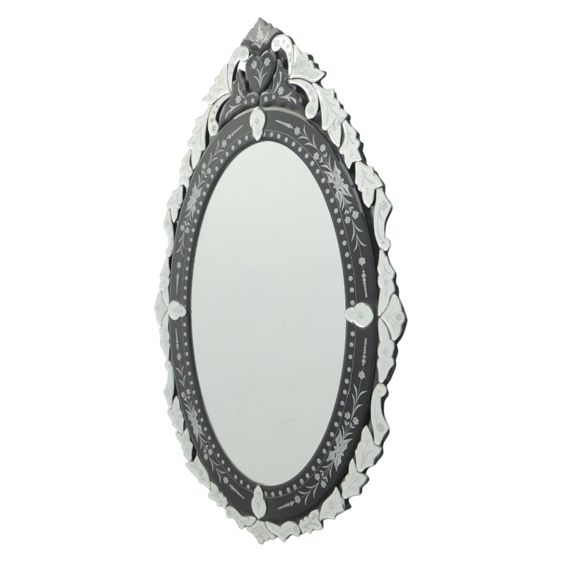 20th century Venetian style oval mirror, the central mirror plate enclosed by an ebonised border decorated with engraved floral trails and dotted reserves, the outer edge applied with shaped and etched glass leaves and scrolling foliage